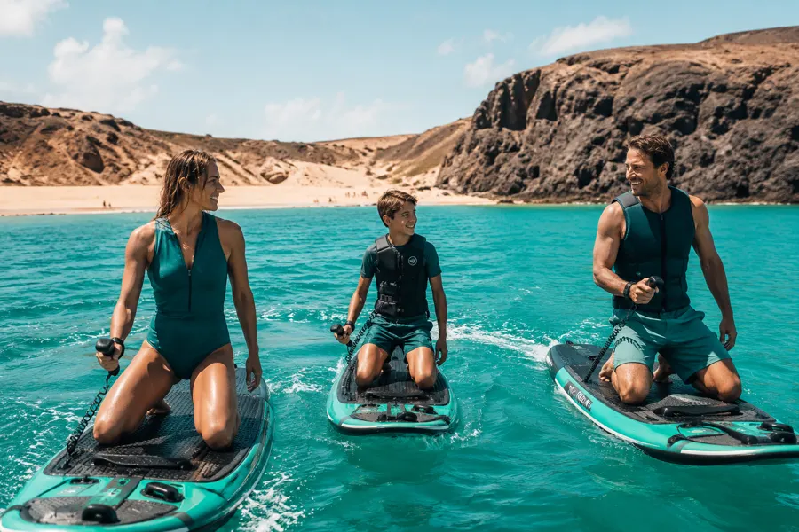 Familie auf eSurf-Boards im türkisfarbenen Wasser von Papagayo, Lanzarote