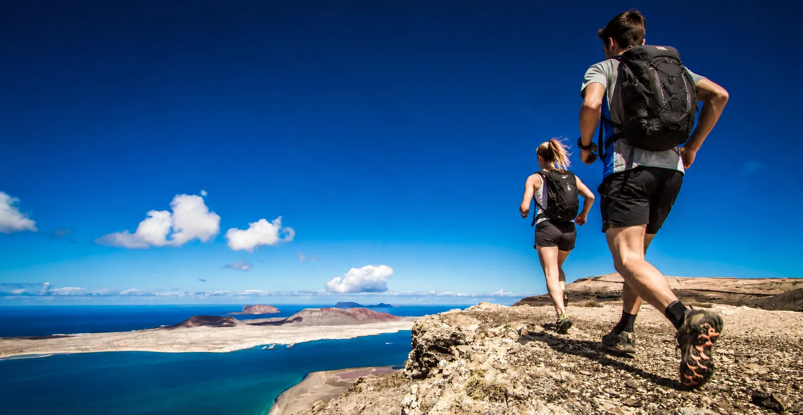 Senderistas corriendo por la cresta del Risco de Famara con vistas a La Graciosa